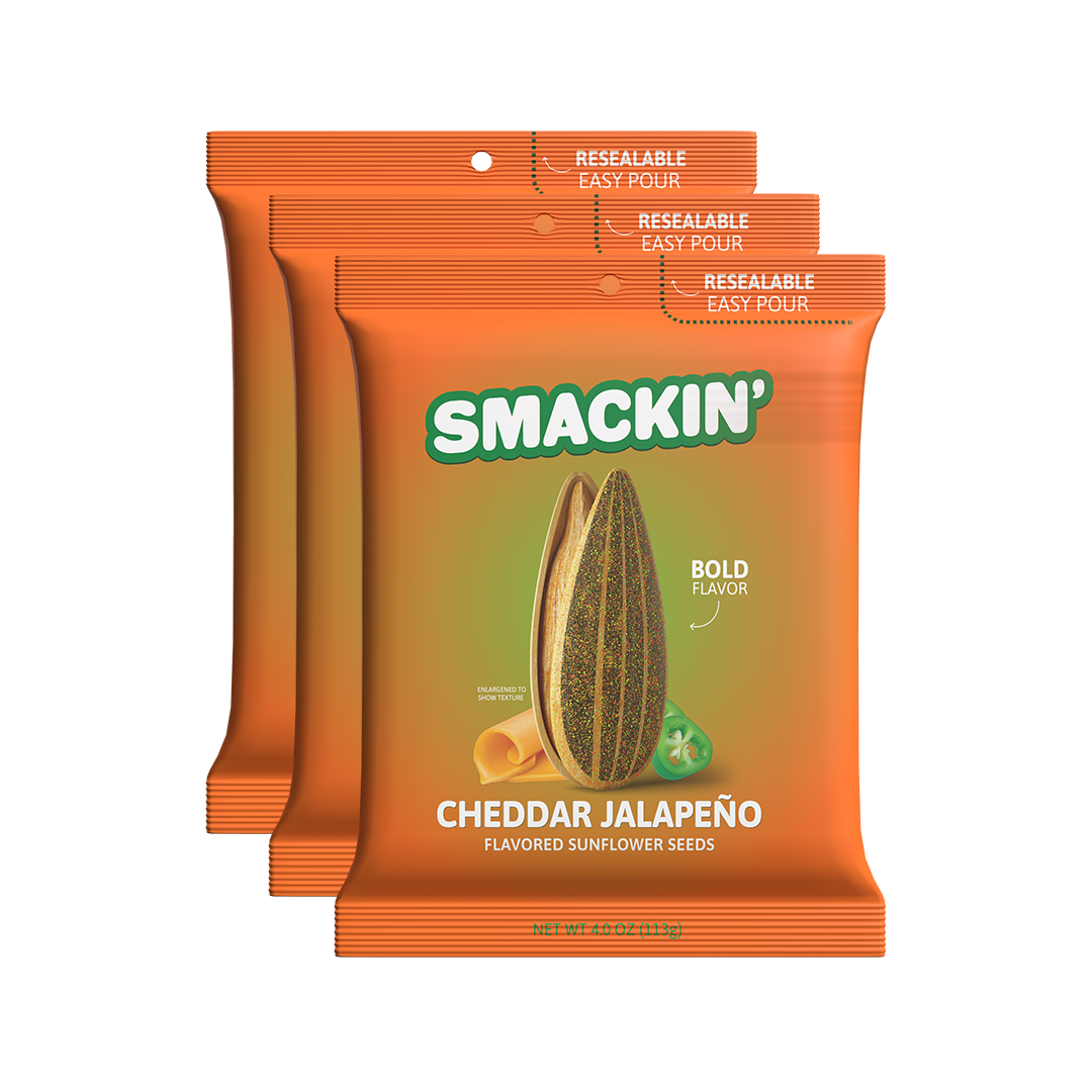 Product packaging featuring three bright orange Smackin' Cheddar Jalapeño Flavored Sunflower Seeds bags each with a green logo a large sunflower seed bold flavor text a yellow cheddar curl and a green jalapeño slice and "Resealable Easy Pour" printed at the top