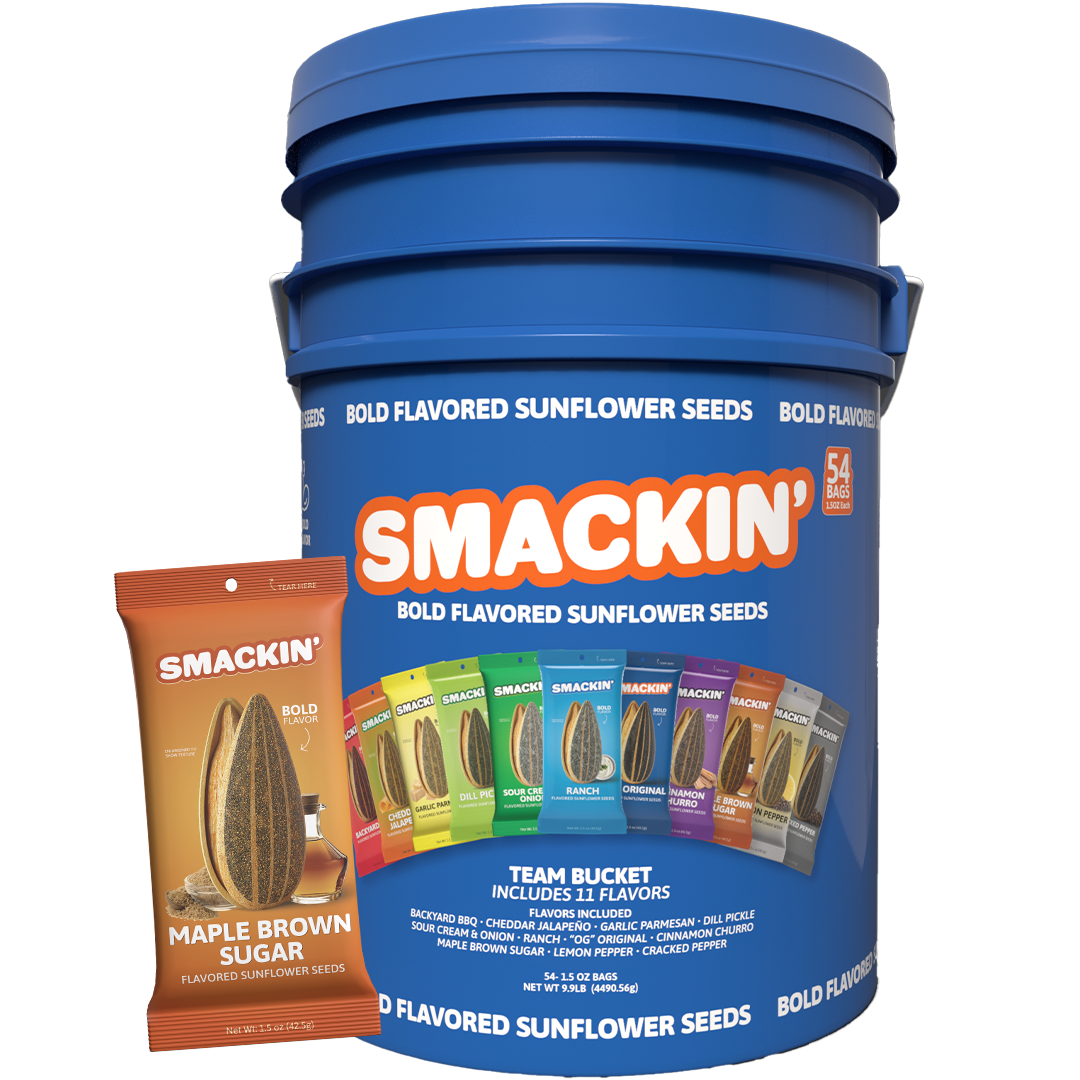 Product photography showing a prominent blue Smackin' Bold Flavored Sunflower Seeds Team Bucket with 54 bags, displaying 11 colorful flavor options like Ranch and Dill Pickle, positioned next to a smaller orange Maple Brown Sugar flavored bag featuring a sunflower seed and syrup image
